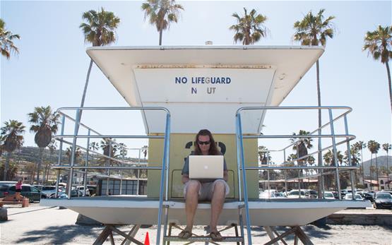 Christopher Wilson seating in a lifeguard tower with a laptop on his lap