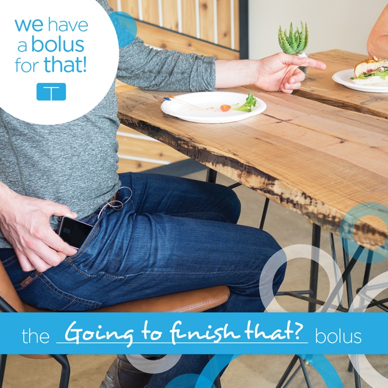 Two persons seating a wooden table in a cafeteria. One person have the t:slim X2 insulin pump in pocket. Text Graphics: the going to finish that? bolus; We have a bolus for that!