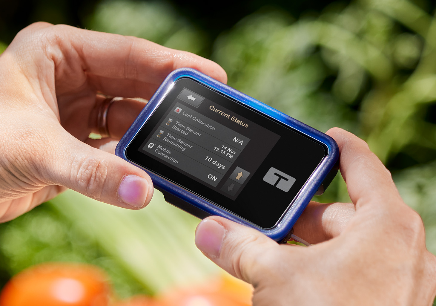 Person holding the t:slim X2 insulin pump showing the Current Status screen