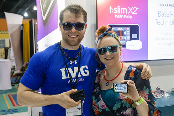 A man and a woman standing in from a t:slim X2 banner  at a conference, both showing their t:slim X2 insulin pump.