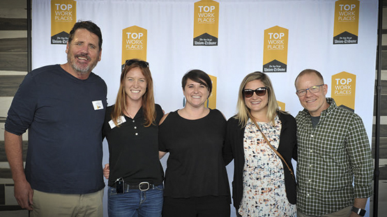 Tandem employees standing and smiling in front of a Top Work Place banner